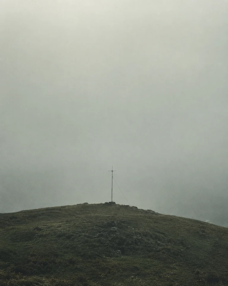 A slender radio antenna on a low grassy hill beneath pale coastal fog